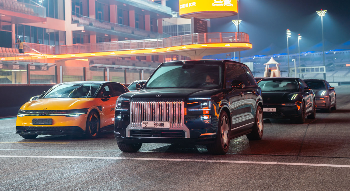Luxury black Zeekr 009 SUV leading a line of high-performance electric cars on an illuminated night race track.